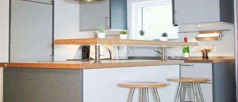 A modern kitchen with a central island, bar stools, stainless steel appliances, and a window providing natural light.