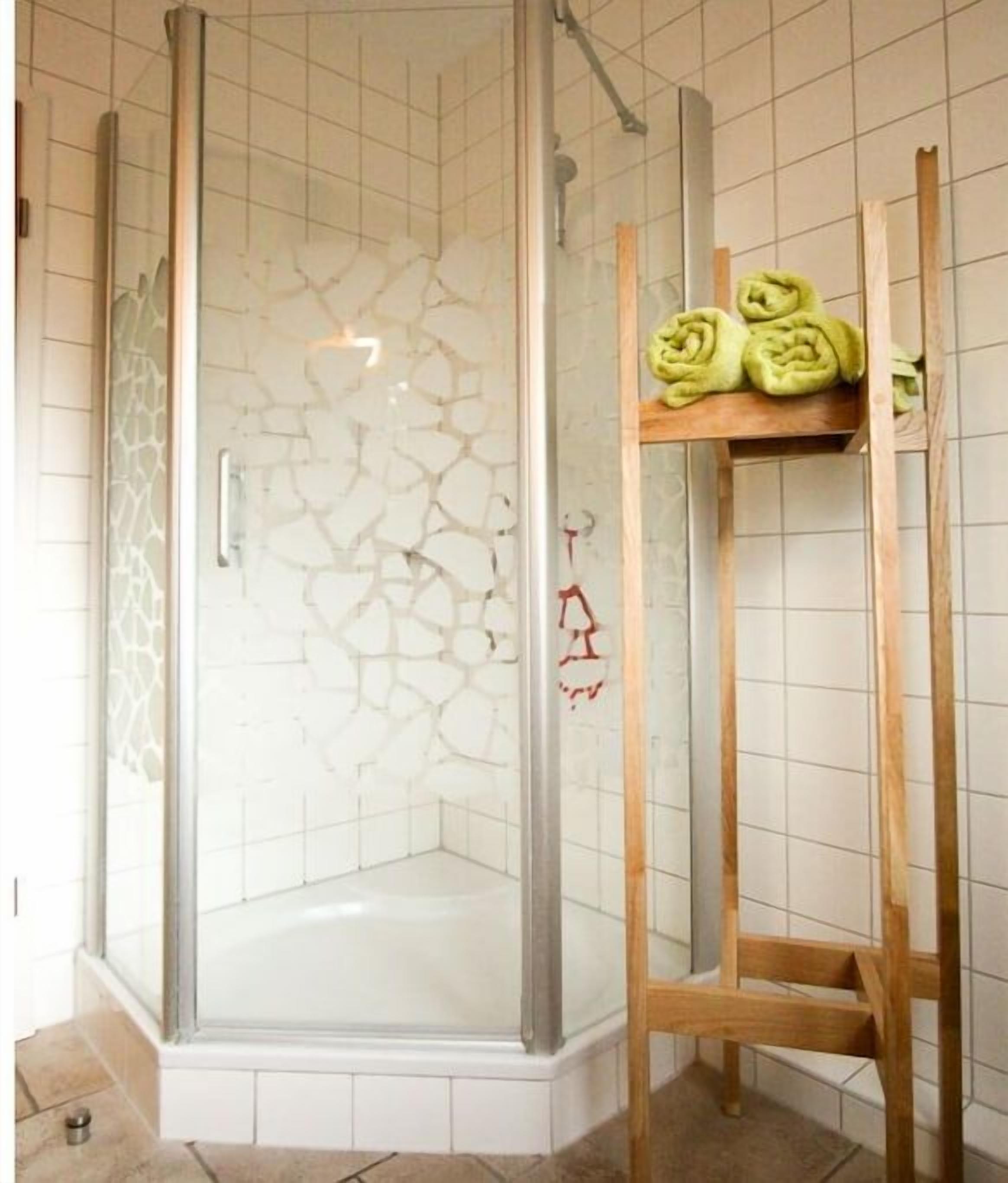 Eine Duschkabine mit Glas, ein gefliester Boden und ein Holzregal mit aufgerollten Handtüchern.
