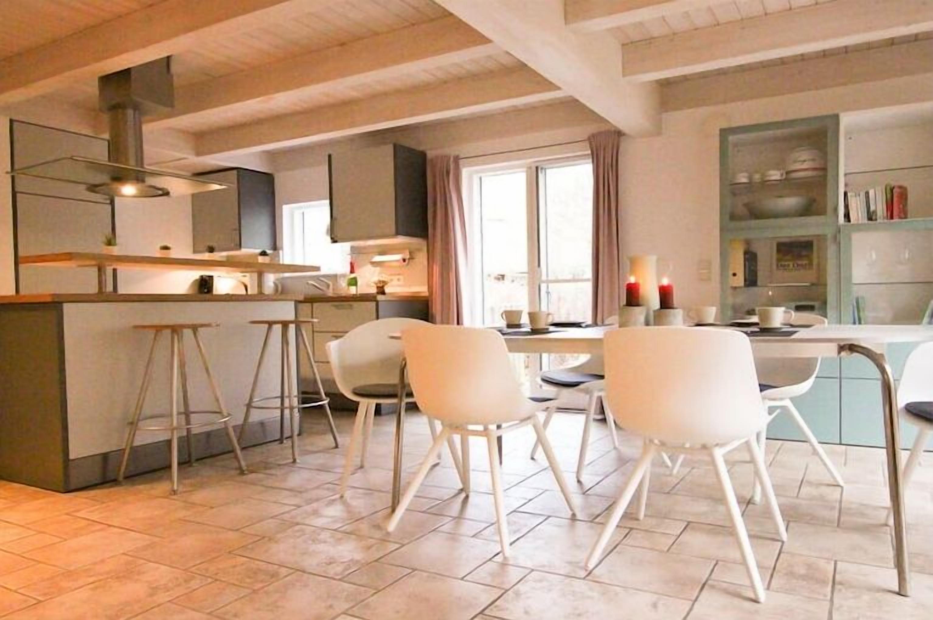 A modern kitchen with a central island, bar stools, and a dining area with chairs.