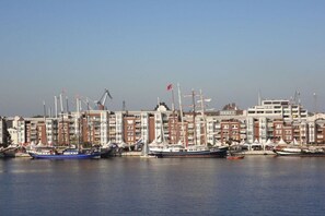 Un port esportiu amb diversos velers amarrats, cel serena i una filera d'edificis al fons.