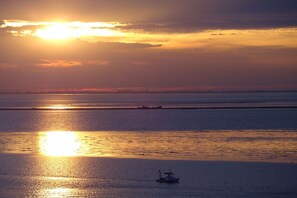 A sunset over a calm body of water with a boat in the foreground. - Holiday apartment with 3 bedrooms (Wilhelmshaven)