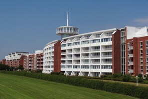 A modern multi-story hotel with a central tower, multiple balconies, and a well-maintained lawn. - Holiday apartment with 3 bedrooms (Wilhelmshaven)