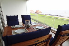 A dining table with four chairs, a glass jar with a plant, and a view of the sea and buildings. - Holiday apartment with 3 bedrooms (Wilhelmshaven)