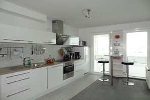 A modern kitchen with white cabinets, stainless steel appliances, and a bar area with stools. - Holiday apartment with 3 bedrooms (Wilhelmshaven)