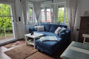 Un salon avec un canapé bleu, une table basse blanche et une vue sur la verdure à l’extérieur.