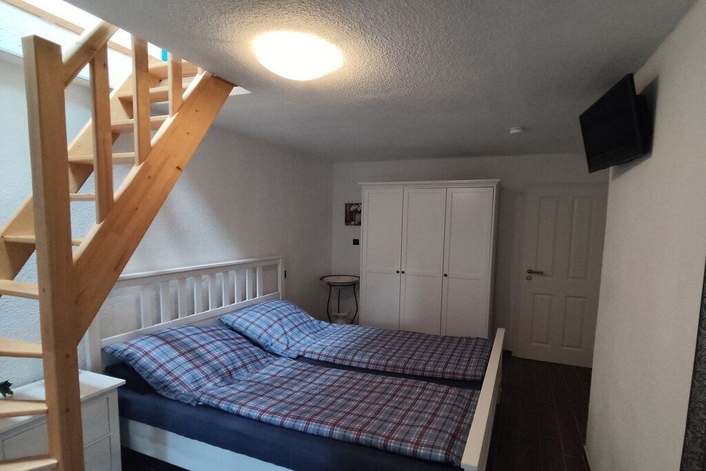 Une chambre à coucher avec un lit, une armoire blanche, une petite table et un téléviseur fixé au mur.