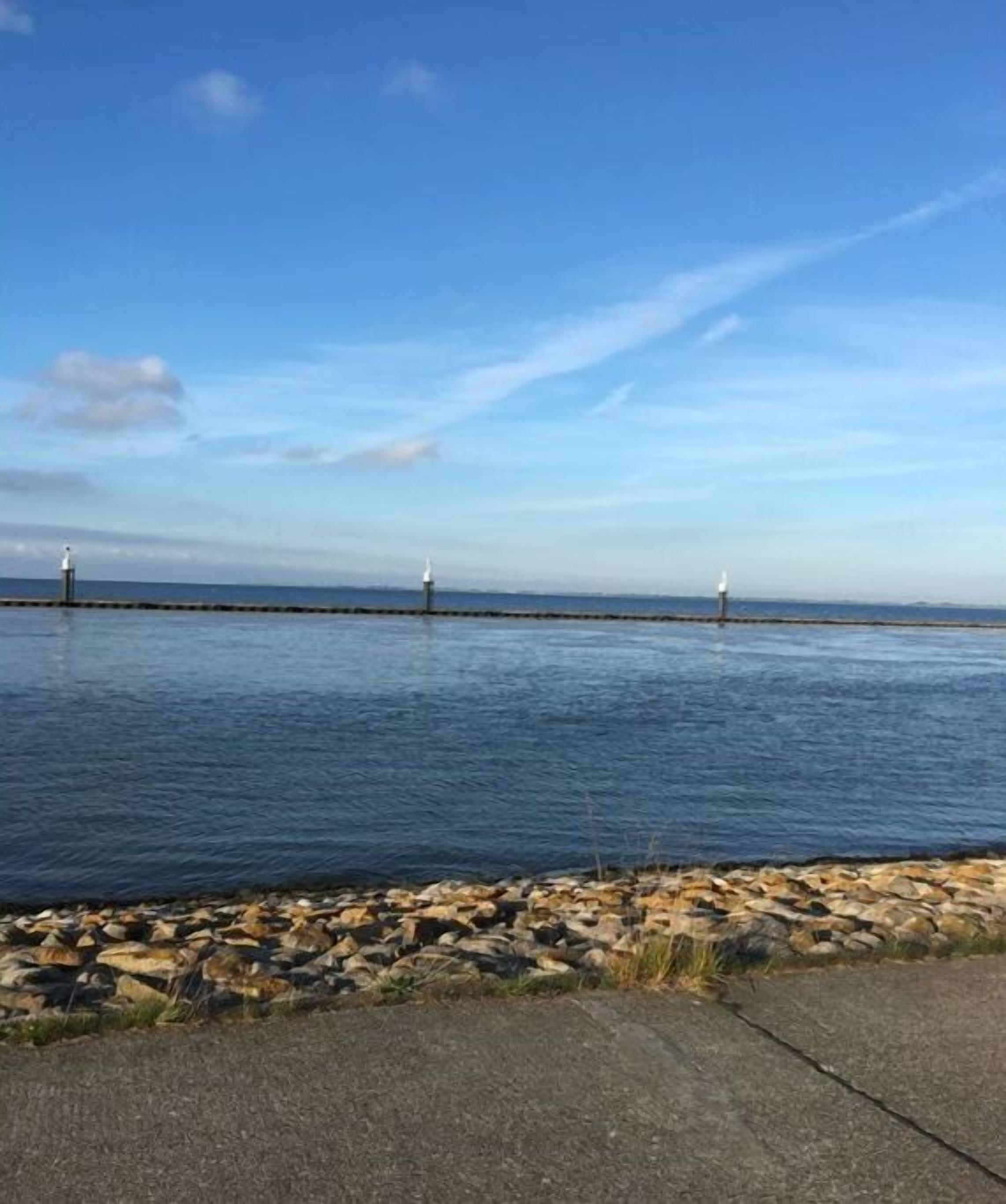 A calm waterfront with a paved walkway and three lighthouses in the distance.