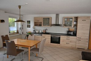 Une cuisine moderne avec des meubles en bois, un four noir et un coin repas comprenant une table et des chaises en bois.