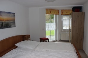 Ein Schlafzimmer mit einem großen Bett, einem Holzschrank, einem kleinen Hocker und einem Fenster mit Blick ins Freie.
