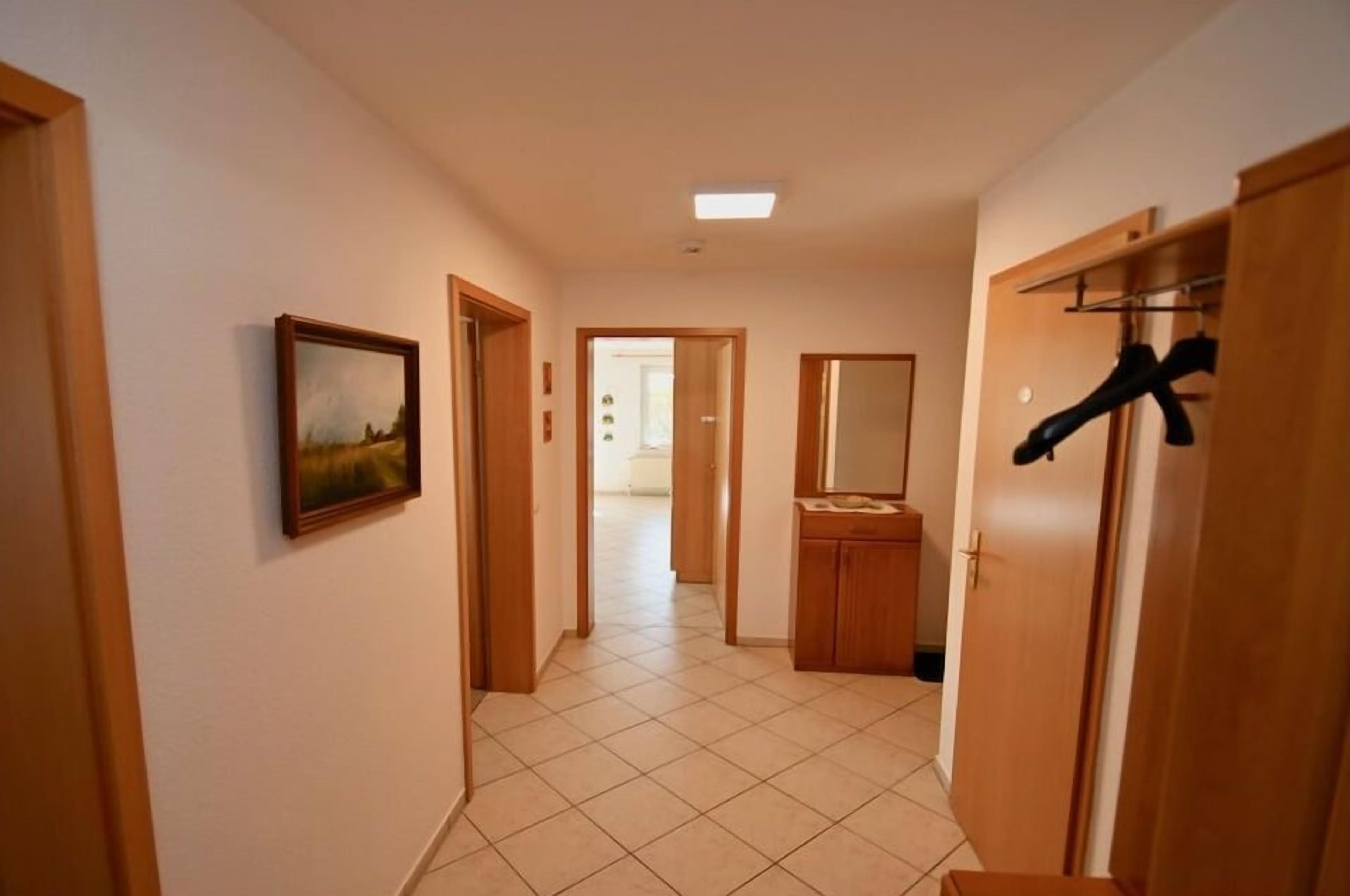 Un couloir avec des portes en bois, un sol carrelé, un tableau accroché au mur et un porte-manteau.