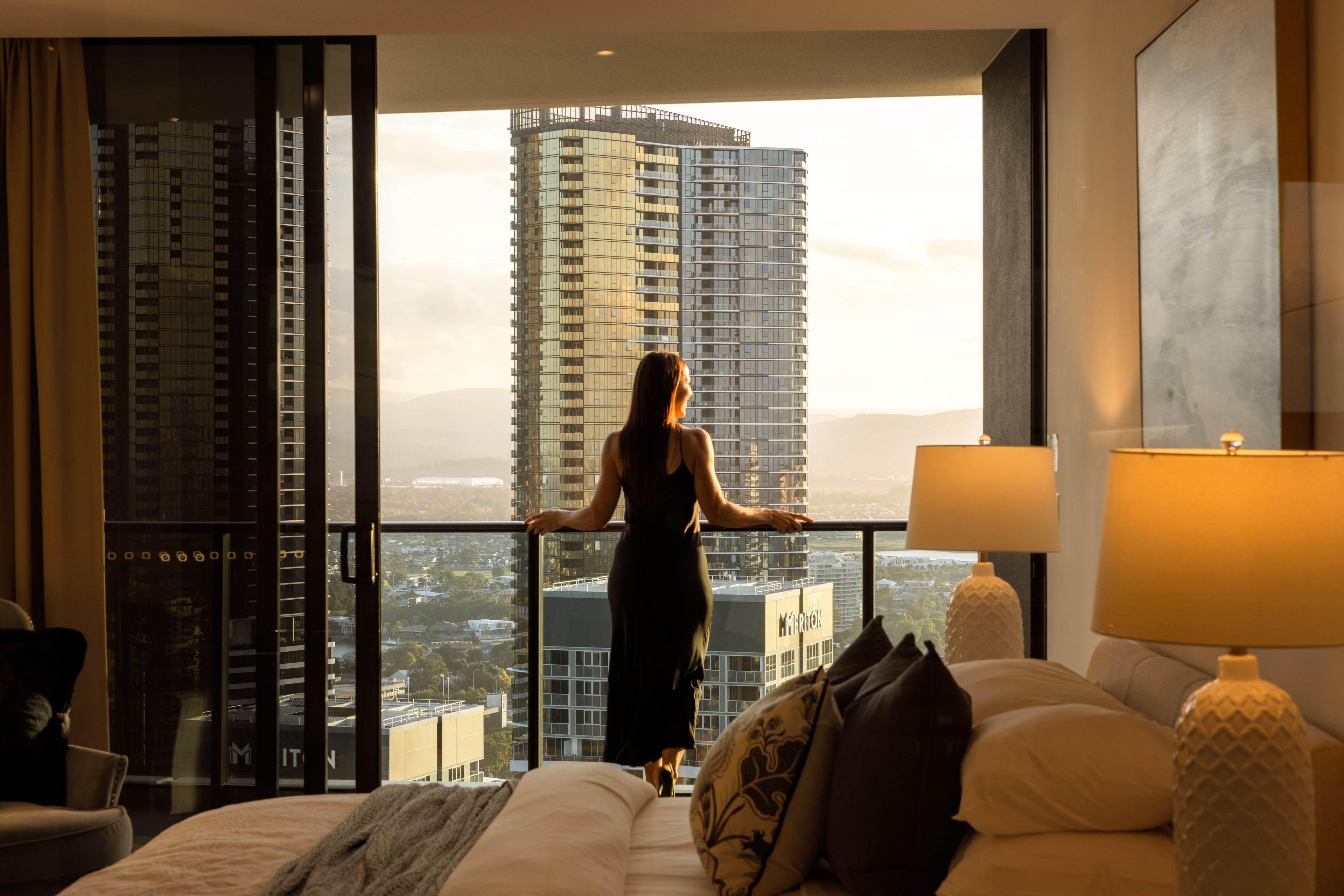 A hotel room with a large window, a bed, a chair, and a lamp.