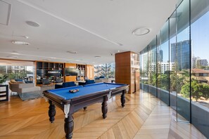 A modern living room with a pool table, a fireplace, and a large window overlooking a cityscape. - Two Horizons by Aryve (Broadbeach)