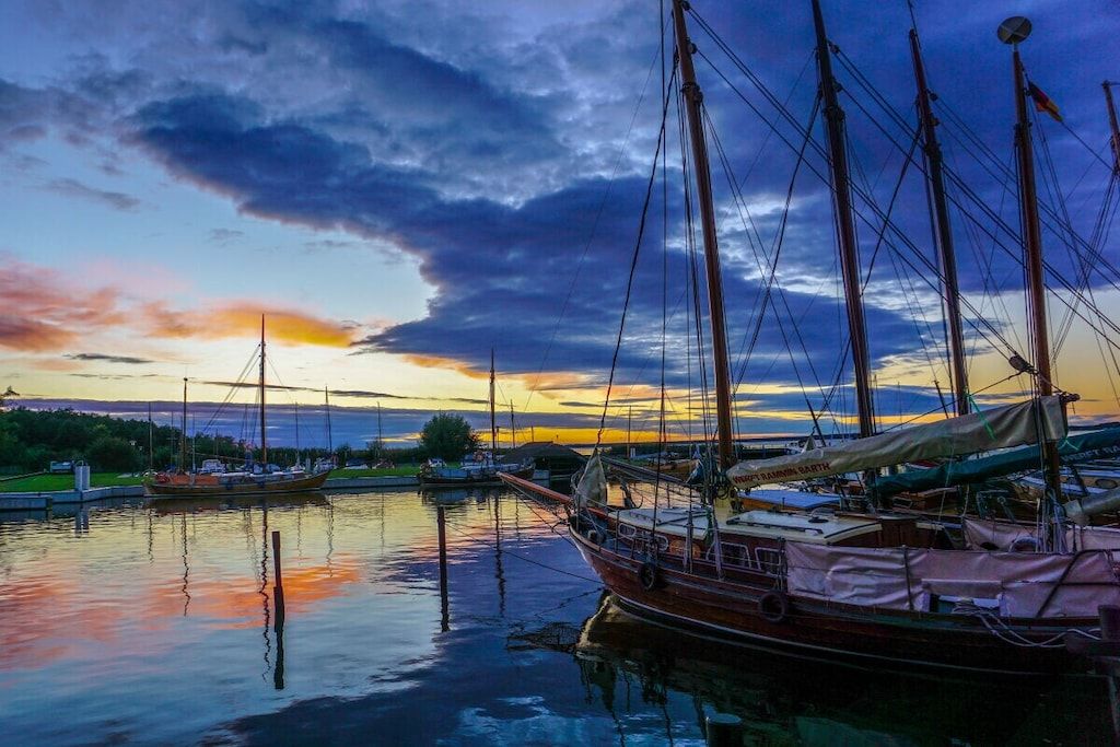 A marina with multiple boats docked, calm water, and a sunset in the background.