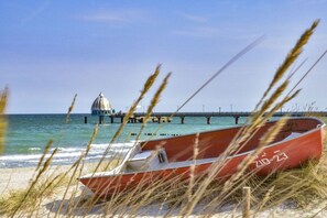 A beach with a red boat, a pier, and a structure in the distance. - Holiday home with 2 bedrooms (Fuhlendorf)