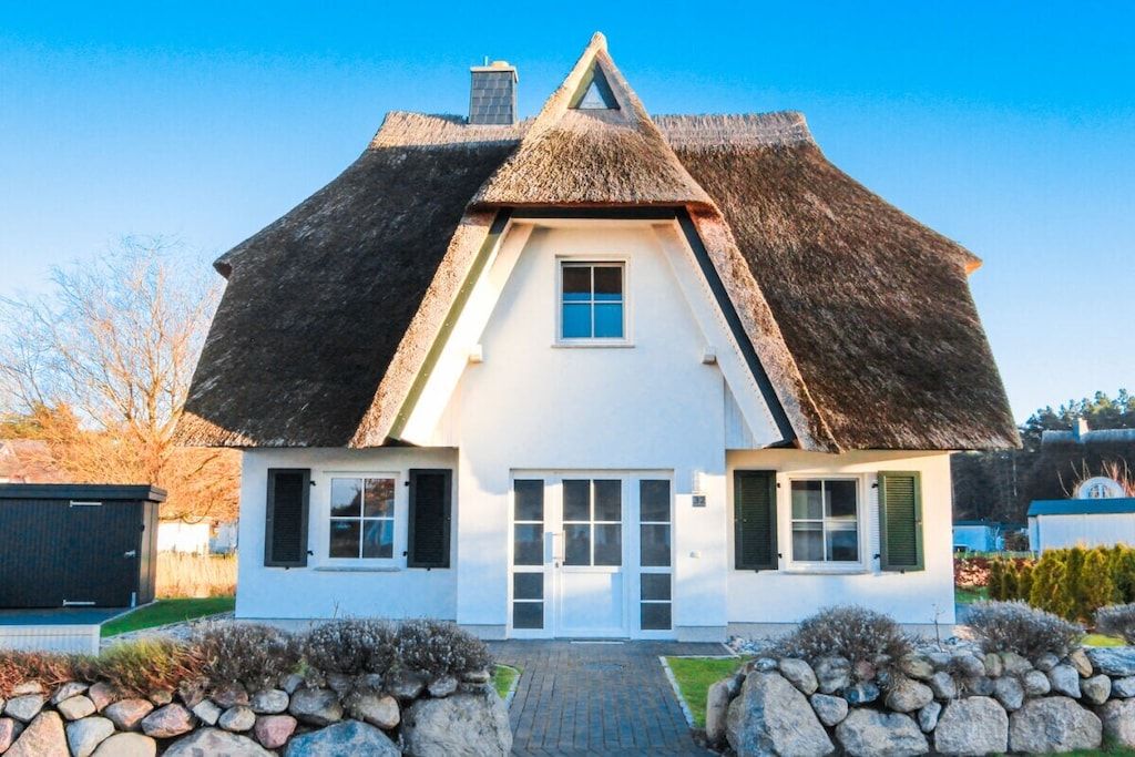 Une maison blanche avec un toit de chaume, une porte centrale et une petite fenêtre.