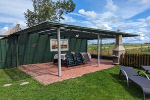 Ein überdachter Patio-Bereich mit Tisch, Stühlen, einem Grill und Blick auf die umliegende Landschaft.
