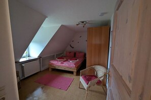 Ein Schlafzimmer mit schrägem Dach, einem Bett mit roter Bettwäsche, einem Korbstuhl und einer Heizung.