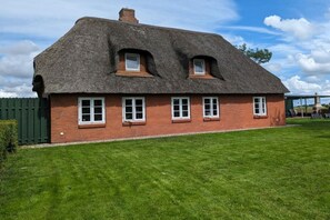 Ein traditionelles Backsteinhaus mit einem Reetdach und zahlreichen Fenstern.