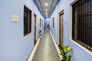 A hallway with blue walls, metal bars on windows, and a potted plant on the right. - Hotel Shree Rudraksha (Varanasi)
