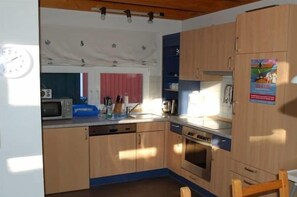 A compact kitchen with wooden cabinets, a microwave, a sink, and a stove. - Holiday home with 2 bedrooms (Ostseebad Prerow)