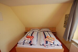 Ein Einzelbett mit gestreifter Bettwäsche und einem hölzernen Kopfteil in einem Zimmer mit schräg verlaufender Decke.
