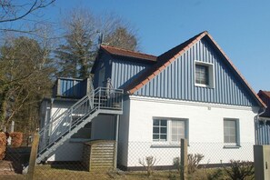 Ein zweistöckiges Haus mit einer Metalltreppe, die zu dem oberen Stockwerk führt, einem eingezäunten Garten und blauem Himmel.