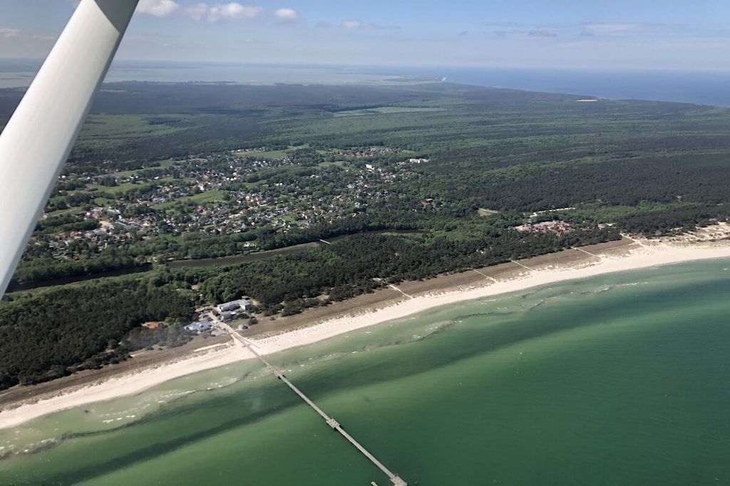 Vista aérea de una zona costera con playa, un pueblo pequeño y una región boscosa.