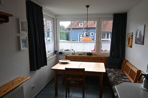 A room with a dining table, bench seating, a window with curtains, and a view of a house outside. - Holiday home with 3 bedrooms (Ostseebad Prerow)