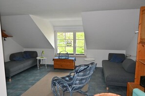 Ein modernes Wohnzimmer mit zwei Sofas, einem Schaukelstuhl, einem kleinen Holztisch und einem Fenster mit Blick auf Grünflächen.