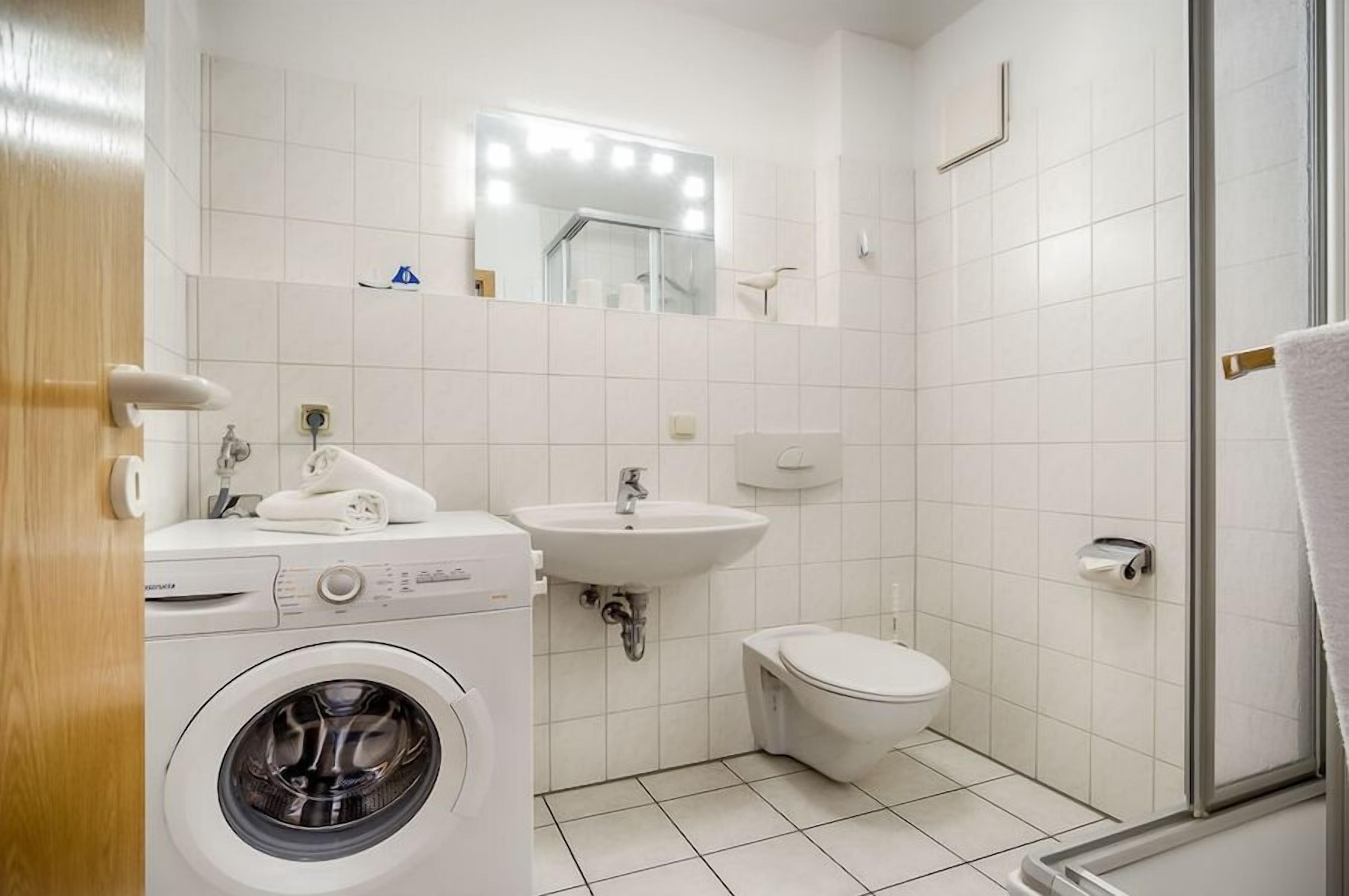 Een kleine badkamer met een wasmachine, wastafel, toilet en een douchecabine van glas.
