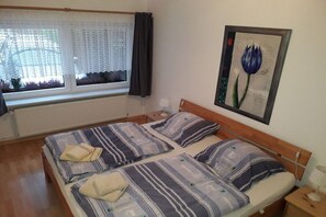 Cama de casal com roupa de cama listrada, janela com cortinas, radiador e quadro na parede.