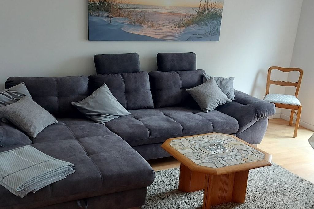 A modern living room with a sectional sofa, a wooden coffee table, and a painting of a beach scene.