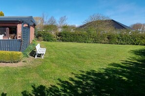 Ein grünes Rasenstück mit Bank, einem Backsteinhaus und einer Hecke.