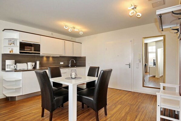 A modern kitchen with white cabinetry, a dining table with chairs, and a built-in oven. - House by the Park Apartment 32 (Kühlungsborn)