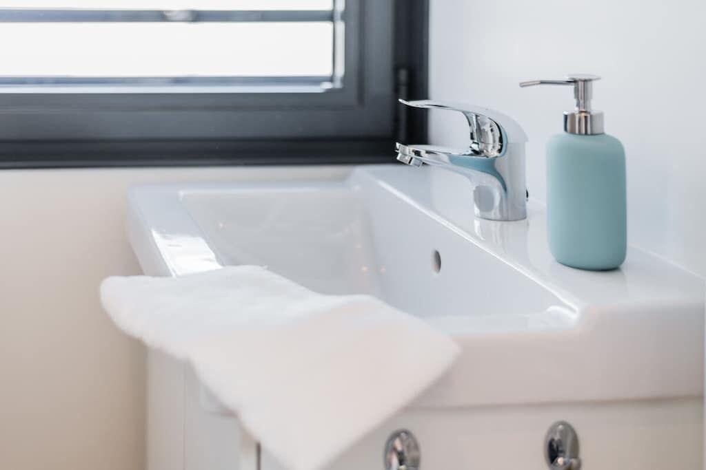 A bathroom with a white sink, a faucet, a soap dispenser, and a towel.