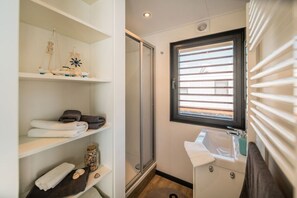 A bathroom with a shower, a sink, and shelves with towels and toiletries.