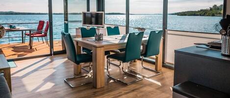 A modern dining area with a view of the water, a television, and a kitchen area.