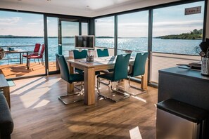 A modern dining area with a view of the water, a television, and a kitchen area.