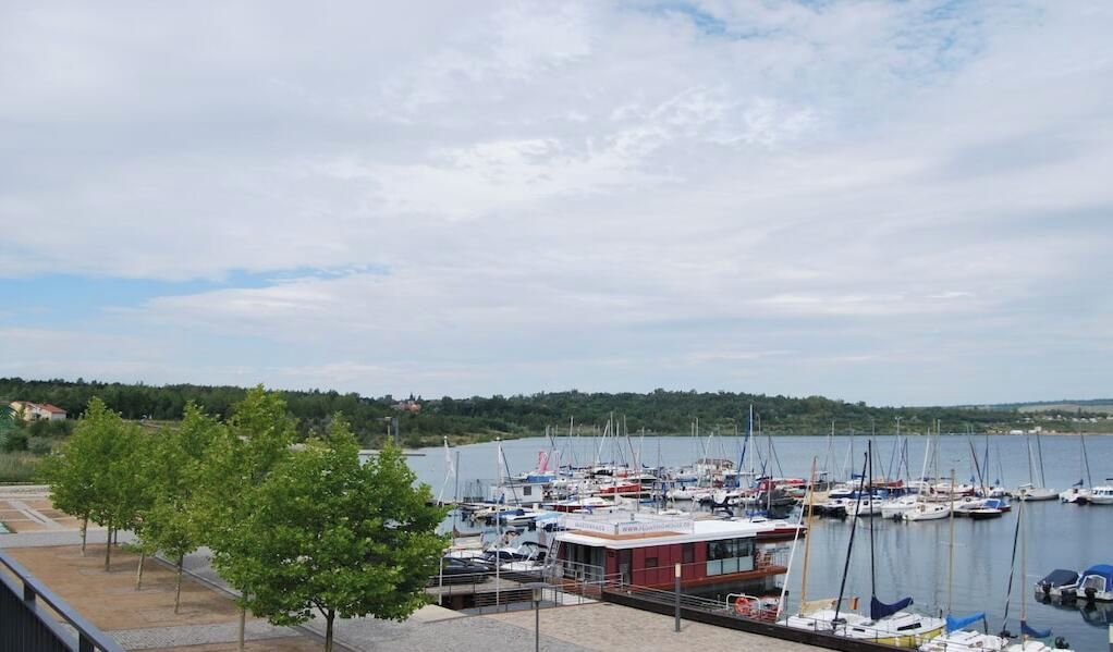 A marina with boats docked, a building with a red roof, and a tree-lined path.
