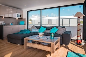 A modern living room with a sofa, coffee table, and a view of a building through large windows.