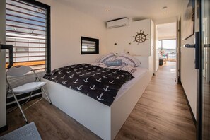 A modern bedroom with a bed, a chair, a window with blinds, and a view of the outdoors.