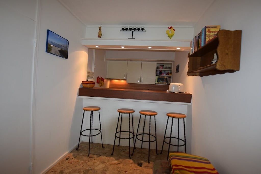 Una cocina compacta con barra, taburetes y un pequeño estante con libros.