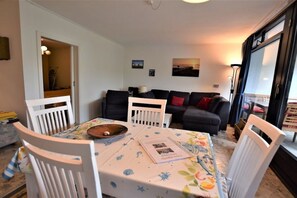 A living room with a dining table, chairs, a sofa, and a large window. - Holiday apartment with 1 bedroom (Hohwacht (Ostsee), Deutschland)