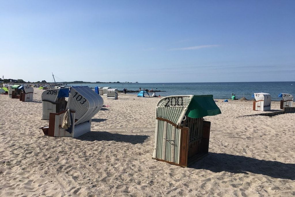 Des cabanes de plage numérotées, disposées sur une plage de sable, avec la mer en arrière-plan.