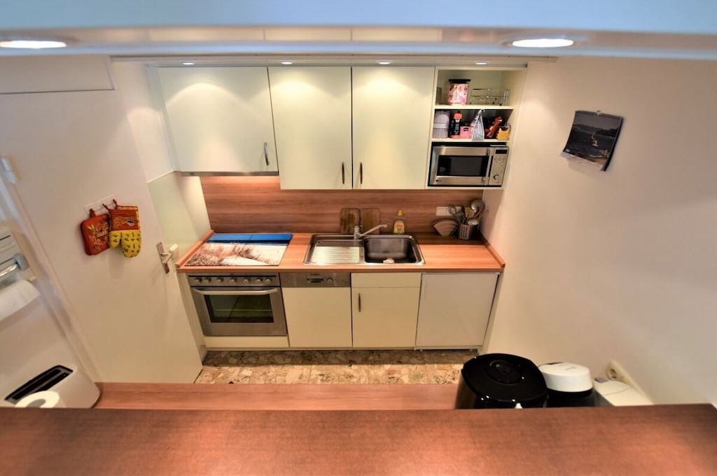 Een kleine keuken met witte kastjes, een magnetron en een kookplaat.