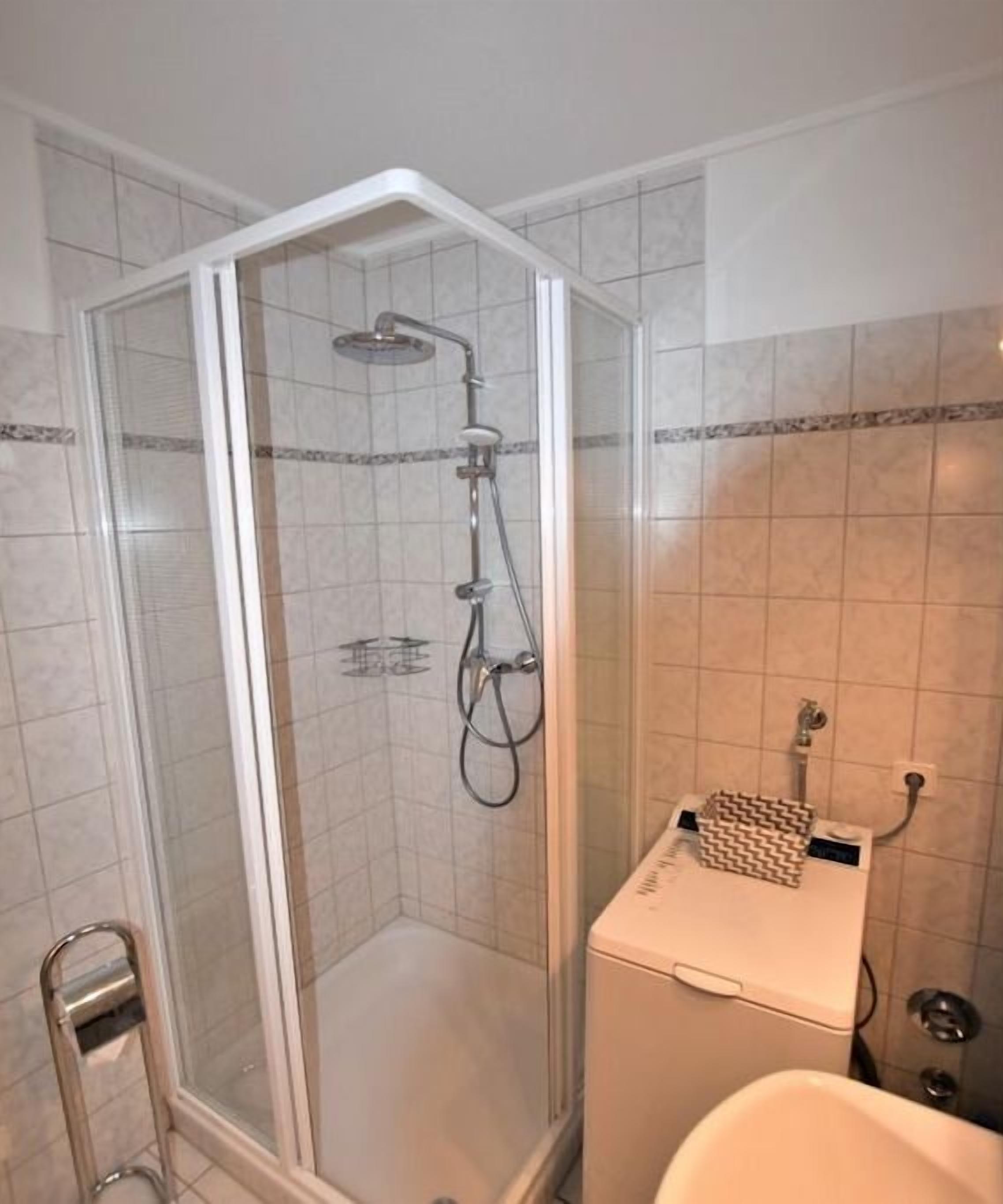A shower with a glass enclosure, a handheld showerhead, and a wall-mounted faucet.
