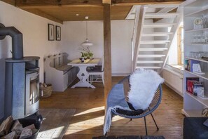 A cozy room with a wood-burning stove, a dining area, a chair with a fluffy throw, and a bookshelf. - Holiday home in Schlei with 2 bedrooms (Klappholz)