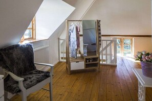 Una habitación con piso de madera, una silla blanca, un perchero y una escalera que sube a un nivel superior.