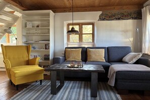 Ein Wohnzimmer mit einem gelben Sessel, einer dunklen Couch, einem Holztisch und einem gemusterten Teppich.