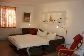 A bedroom with a bed, a chair, a desk, a mirror, and a window with curtains. - Holiday home in Born with swimming pool (Born)